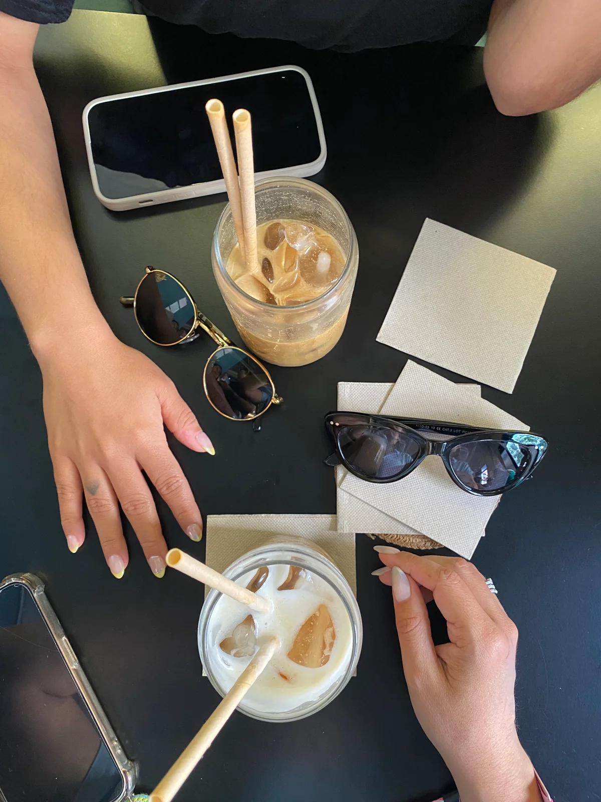 Manos con manicura sobre una mesa de café con dos bebidas frías.