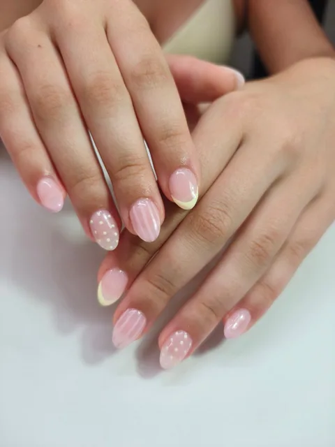 Manicura rosa con rayas, lunares y puntas amarillo pastel.