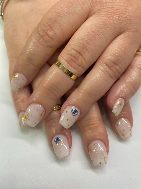 Uñas cortas de base nude con ojos azules y detalles dorados.